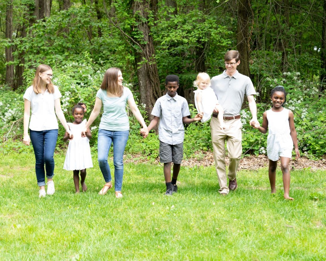 Transracial adopted children holding adoptive parents' hands in a park in Bowling Green, Ohio