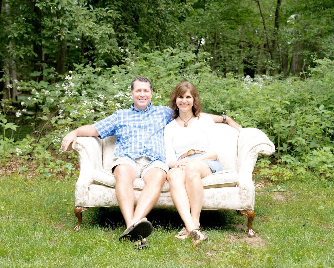This is Stacy and Jeff smiling and sitting on a sofa. Stacy works for Spirit of Faith Adoptions